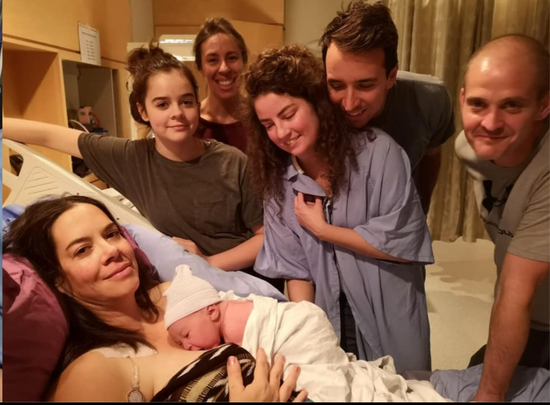 An intimate moment captured for modern baby memory books -intended parents, surrogate, and support team with newborn.